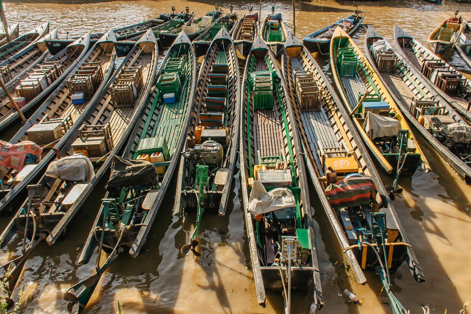 Wooden longboats moored side by side on a muddy riverbank in Southeast Asia