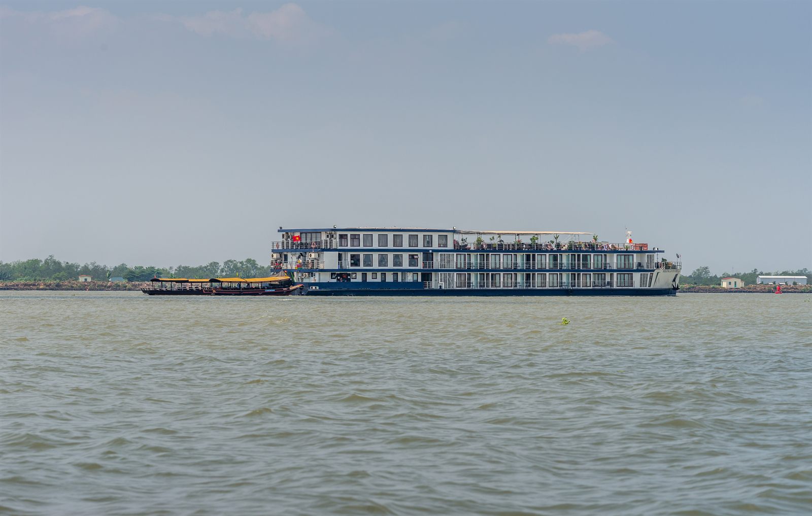 River cruise ship on a wide brown river in Southeast Asia, the style of ship sailing Asia river cruises in 2027